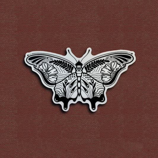 A matte vinyl sticker with a black and white butterfly design, placed on a red background.