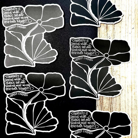 Black and white floral designs with Einstein's quote on a wooden surface.