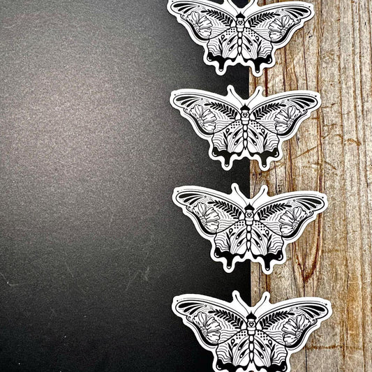 Four black and white butterfly illustrations on a wooden surface.