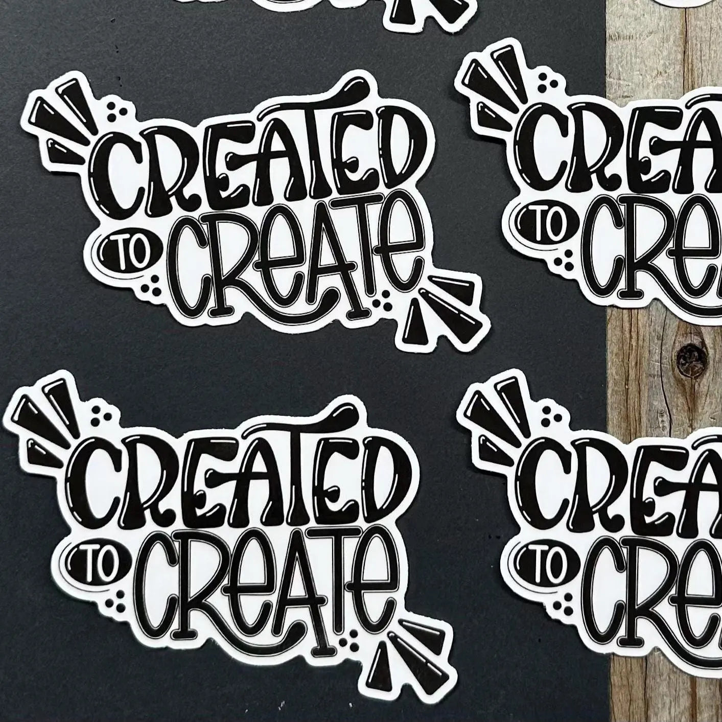 Sticker with 'Created to Create' text on a black background and wooden surface.