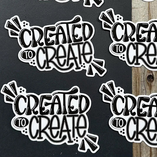 Sticker with 'Created to Create' text on a black background and wooden surface.