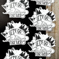 Black and white 'Let's Go Adventuring Together' stickers on a wooden surface.