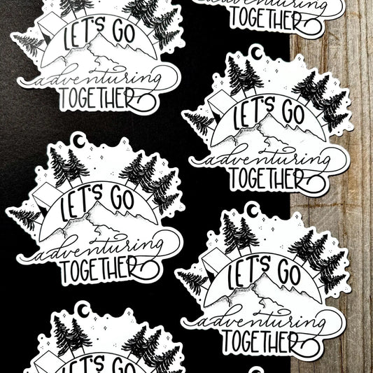 Black and white 'Let's Go Adventuring Together' stickers on a wooden surface.