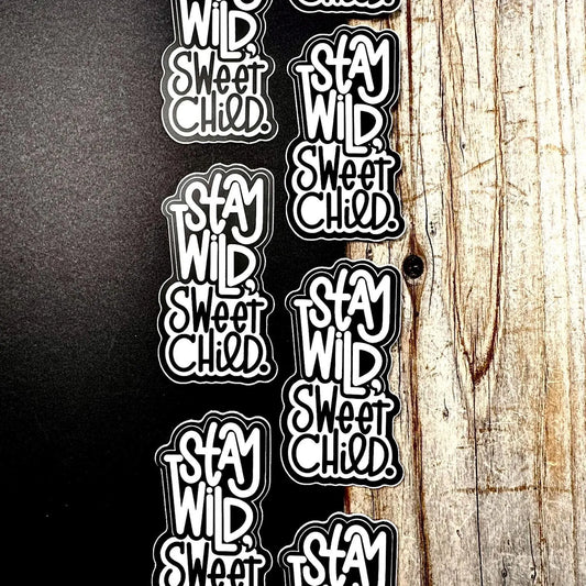 Stickers with 'Stay Wild, Sweet Child' text on a wooden surface