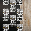 Repeating pattern of 'Wild and Free' stickers with moth designs on a black and wooden background.