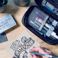 Art supplies flat lay with black Sakura Gelly Roll Glaze pen featured in the center