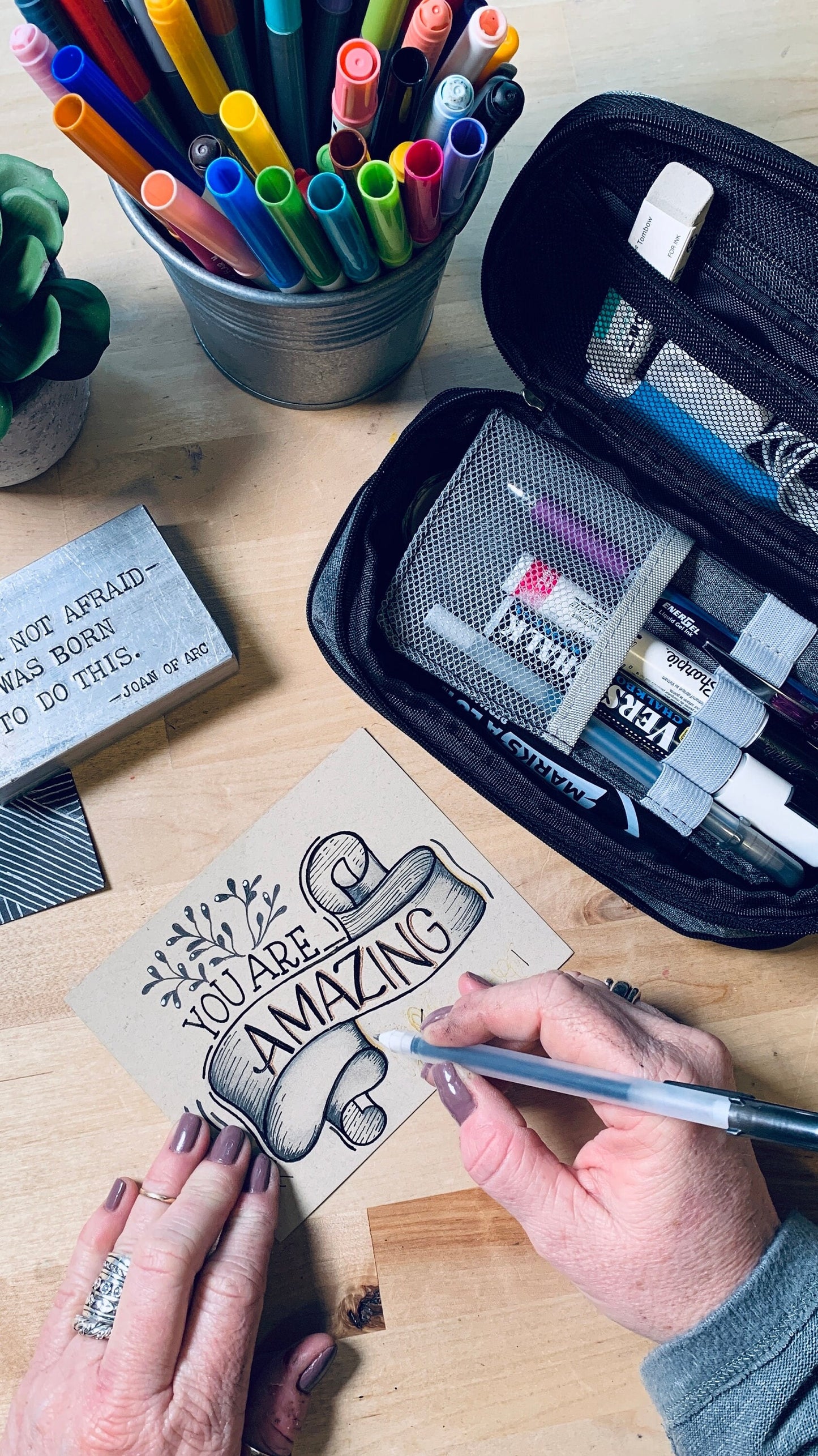 Art supplies flat lay with black Sakura Gelly Roll Glaze pen featured in the center