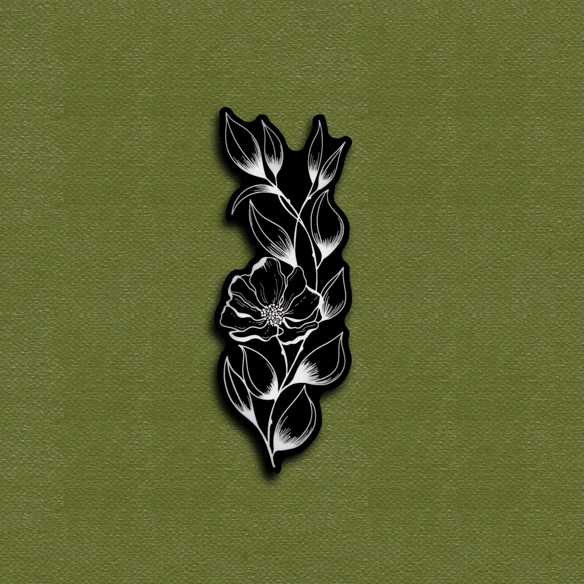 A matte vinyl decal sticker with a tattoo flower design, black and white in color, placed on a green background.